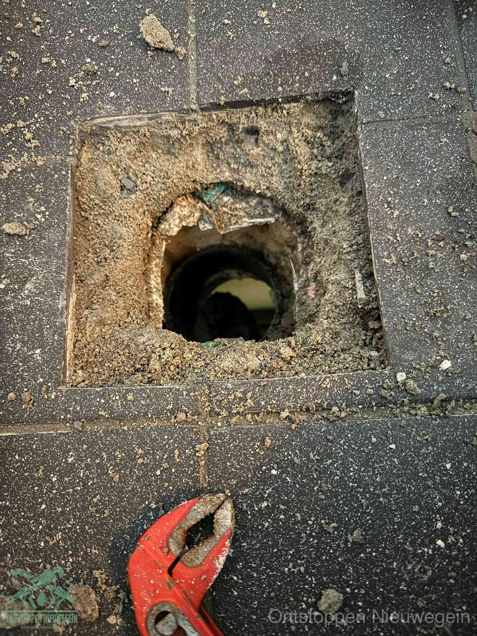 Een geopend rioolputje in een betontegelvloer met losgemaakt rooster en een zichtbare ronde afvoerbuis, het achterhalen waar de afvoerverstopping zit in Nieuwegein