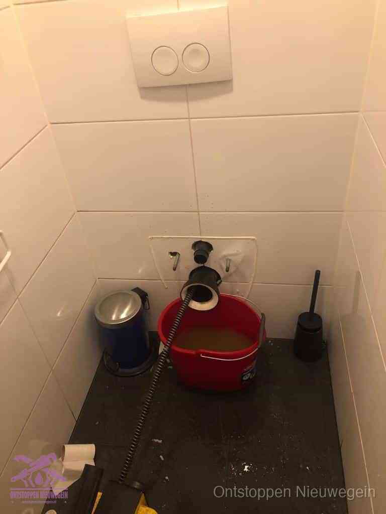 Een ontstopte wand-wc met verwijderde toiletpot waar een ontstoppingsveer in de wanduitgang verdwijnt, het achterhalen waar de verstopping zit in Nieuwegein