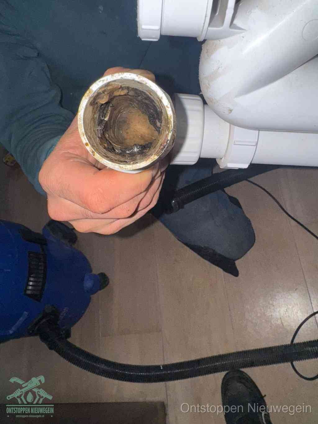 Een hand houdt een losgekoppeld PVC-afvoerbuisstuk vast dat van binnen volledig is dichtgeslibd met vet, vuil en aanslag, de meest voorkomende oorzaak van een verstopte afvoer in Nieuwegein