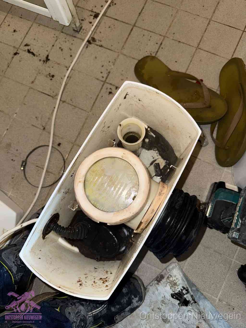 Een gedemonteerde toiletpot op de vloer met ontstoppingsveer en gereedschap ernaast, het verwijderen van een vastzittend voorwerp uit de wc in Nieuwegein