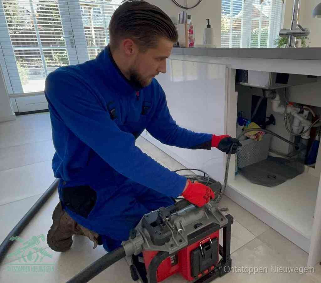 Een monteur met rode handschoenen knielt in een keuken en voert een elektrische ontstoppingsveer in tijdens het professioneel afvoer ontstoppen in Nieuwegein