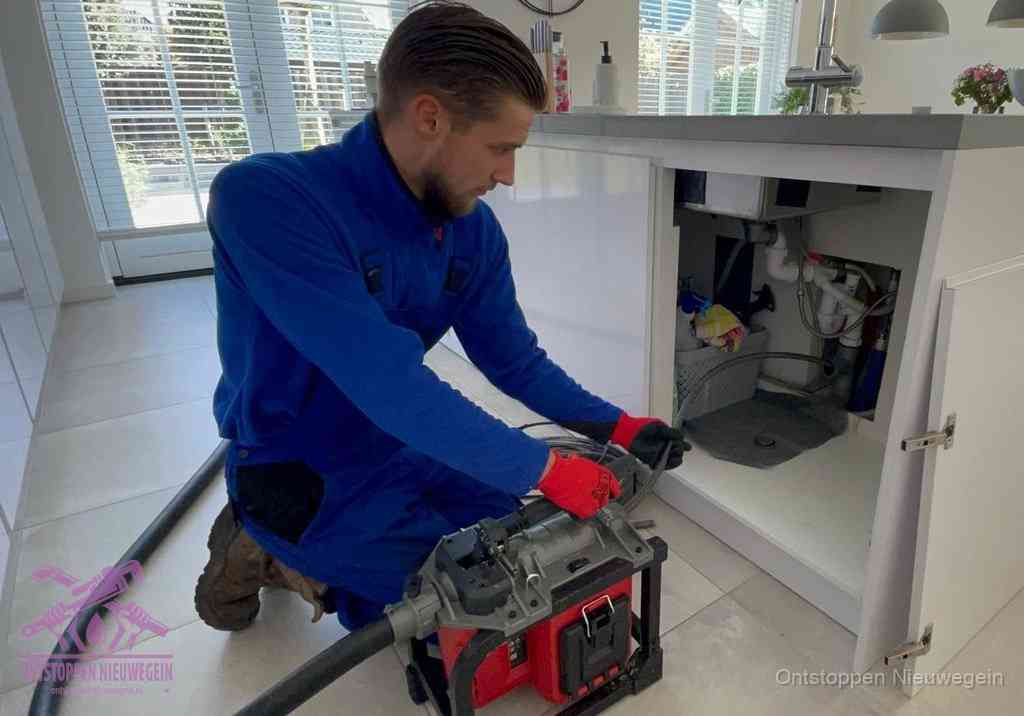 Een monteur voert een professionele elektrische ontstoppingsmachine in de afvoer onder de spoelbak tijdens het gootsteen ontstoppen in Nieuwegein